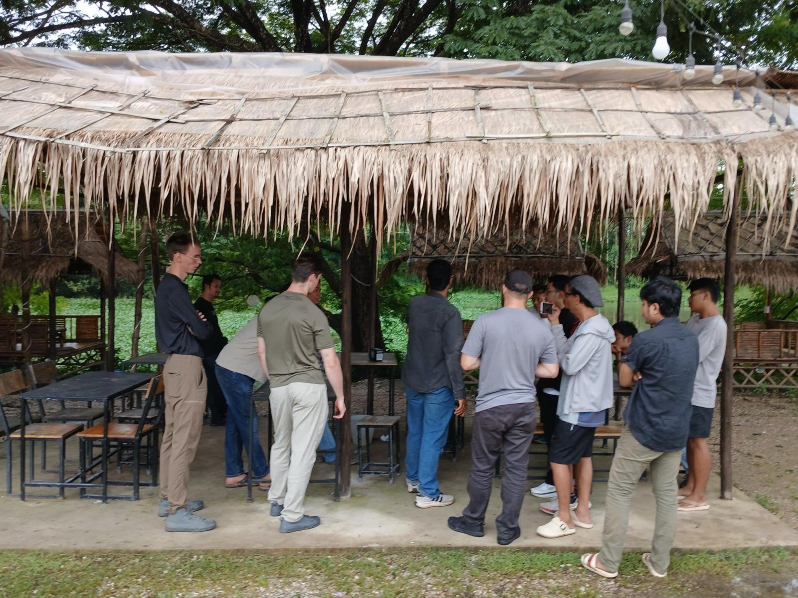 Participants lined up under a thatched shelter watching a demonstration