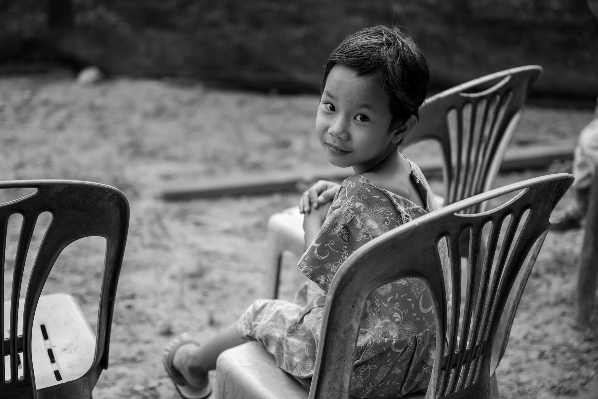 A girl sitting on a plastic chair, smiling at the camera