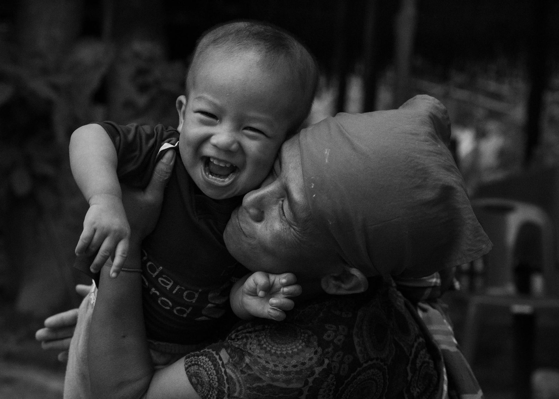 A boy laughing in his grandmother's arms, Burma, 2025