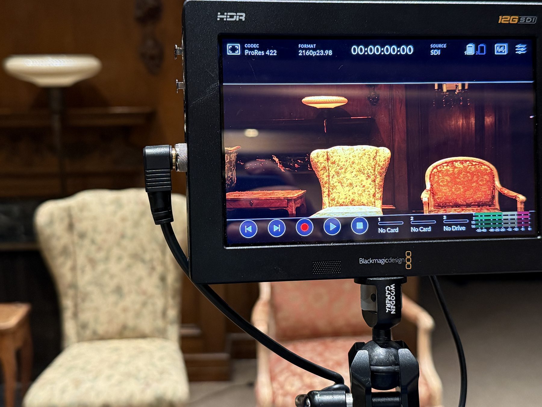 A production monitor on a stand showing a lit interior set, camera feed live